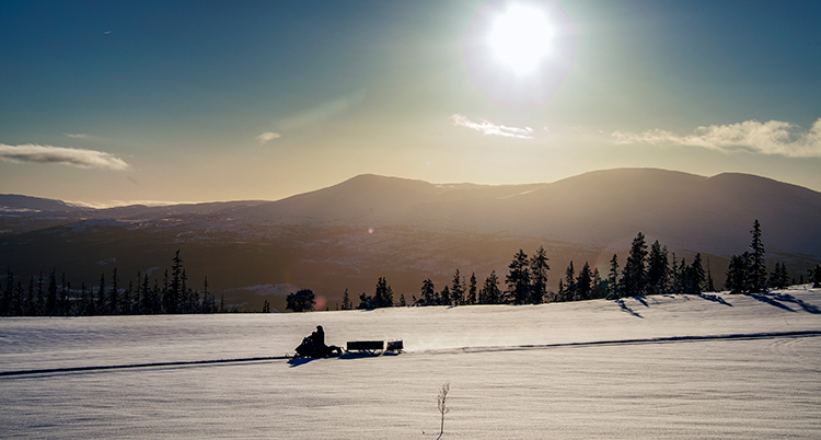 Solen skiner på himlen. Bakom skotern syns fjäll.
