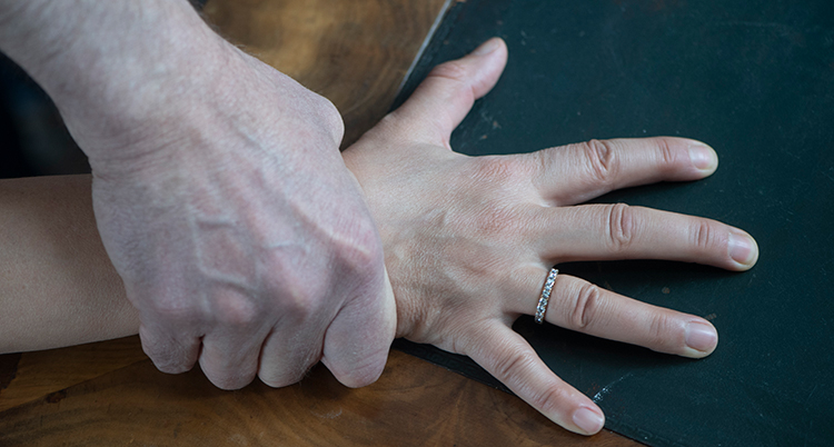 en hand från en person som ser ut att vara en man håller hårt om en hand som ser ut att tillhöra en kvinna. Den hand som blir fasthållen har utspärrade fingrar.