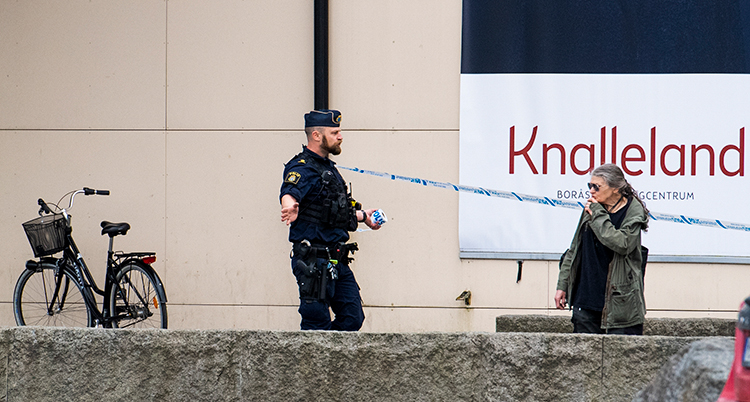 En polis och en till person framför avspärrande band utanför byggnaden.