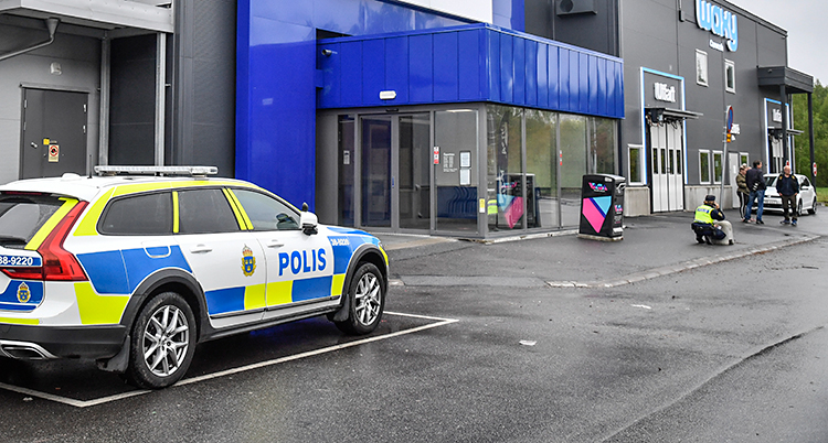 En polisbil står parkerad vid ett köpcentrum. En polis sitter på huk vid en ingång.