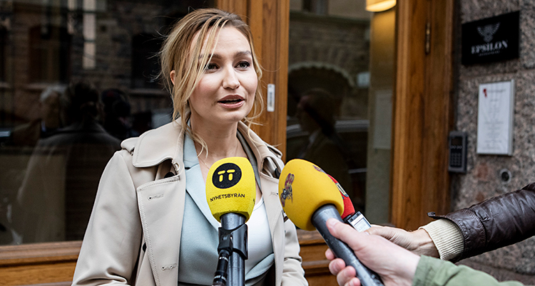 Ebba Busch står utanför en port. Flera journalister sträcker fram mikrofoner mot henne.