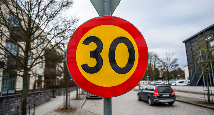 En förbudsskylt där det står 30. Bakom den är en gata med bilar.