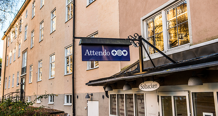 Ett hus med lägenheter i fyra våningar. Närmast kameran är en entré. Ovanför finns en skyld där det står Attendo.