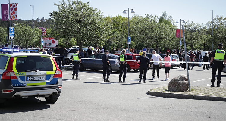 En parkeringsplats med flera bilar. Poliser i gula västar syns och platsen är avspärrad med tejp.