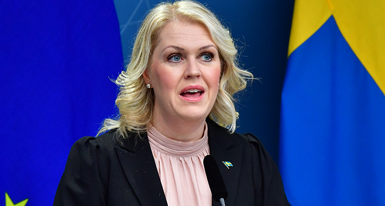 En närbild när Lena Hallengren pratar. Hon tittar bredvid kameran. Bakom henne syns en del av en svensk flagga.