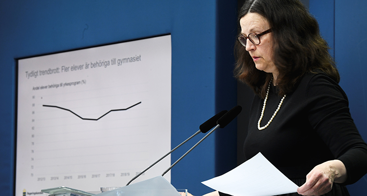 Ministern står i en talarstol med två mikrofoner. Hon tittar ner på några papper. Bakom henne är en bild på väggen som berättar om undersökningen.