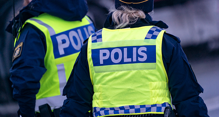 Två poliser med neongula västar, märkta med polis, står med ryggen mot kameran.