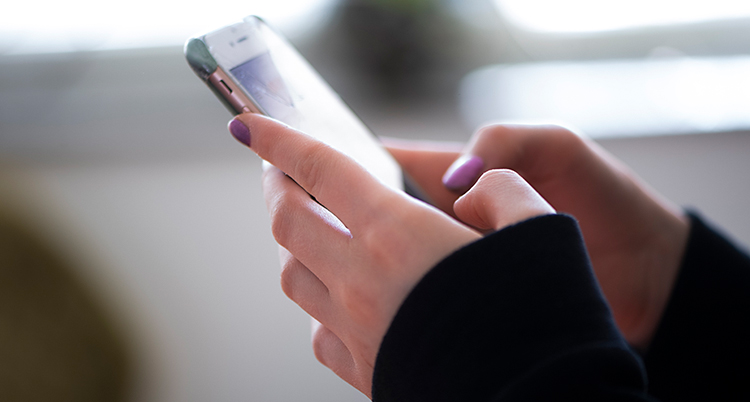 En närbild på två händerna. Händerna håller i en mobiltelefon. Det är lilla nagellack på naglarna.