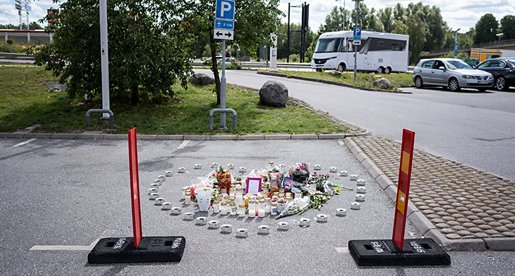 Bilden är tagen på en parkering utomhus. Människor har lämnat ljus och blommor på asfalten.