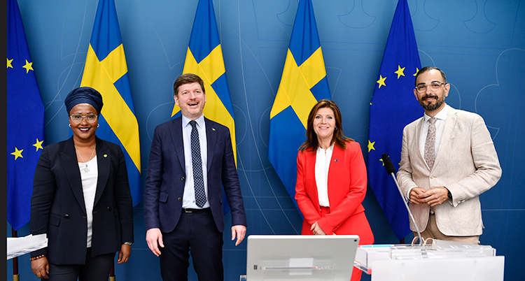 Fyra politiker står bredvid varandra. Bakom dem syns Sveriges flagga.