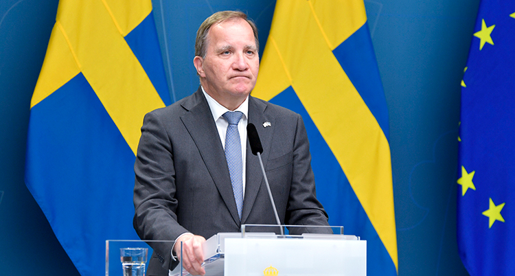 Löfven står framför svenska flaggor. Han ser besviken ut. Mungiporna är neråt.