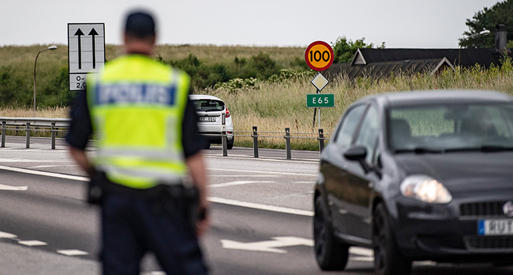 En rygg på en polis. Polisen står vid en väg. Två bilar syns i bakgrunden.