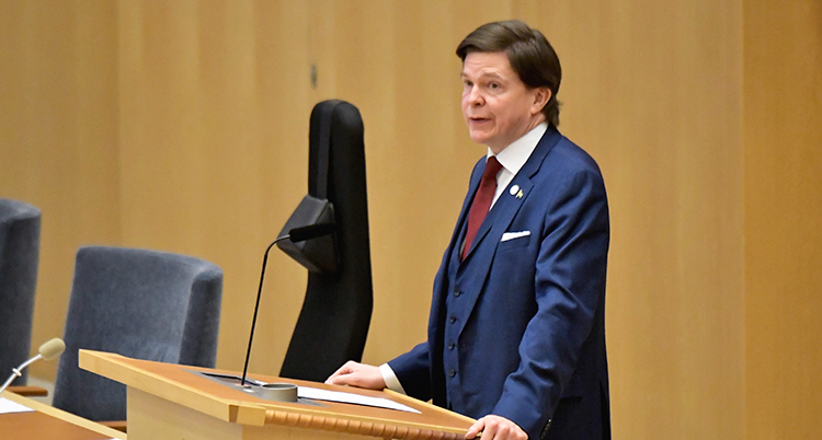 Han står framför en mikrofon i riksdagen.