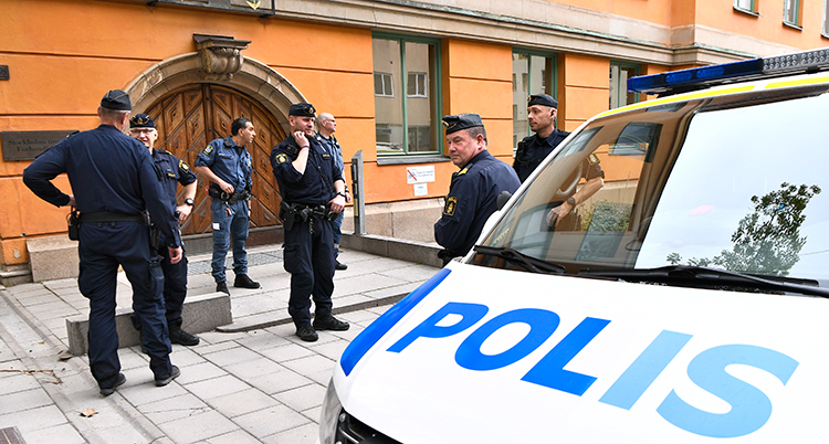 Poliser och en polisbuss märkt med polis står på plattläggningen utanför ett orangefärgat stenhus