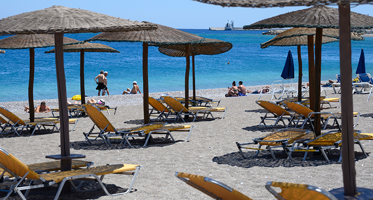 En strand med bara några få människor. På bilden är tomma solstolar under parsoller.