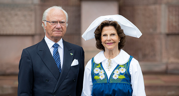 De står bredvid varandra. Han har kostym. Hon har Sverigedräkt i blått.
