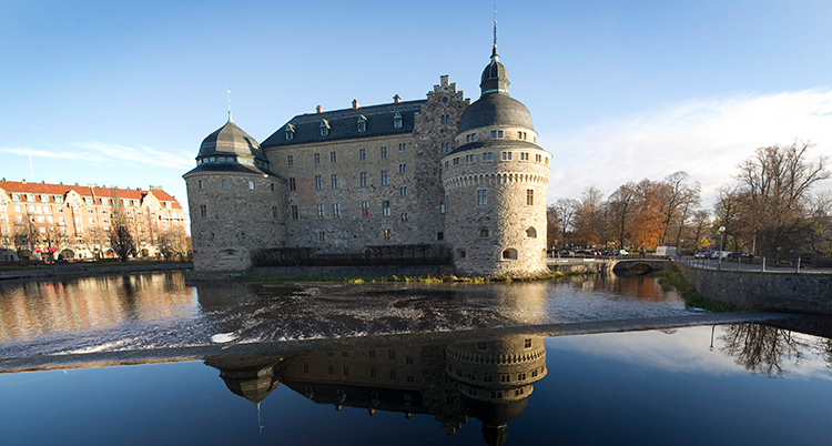 Ett slott omgivet av vatten och andra hus. Himlen är blå.