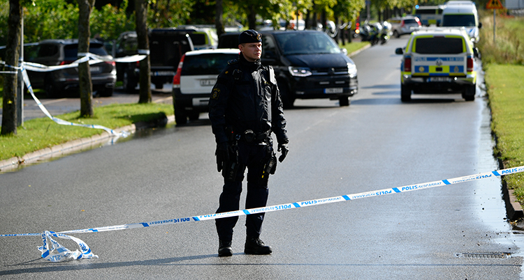 En polis står på en gata bakom en avspärrning.