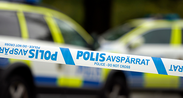 Något har hänt. Poliser har satt upp ett blått och vitt band som spärrar av. Bakom bandet står två polisbilar.