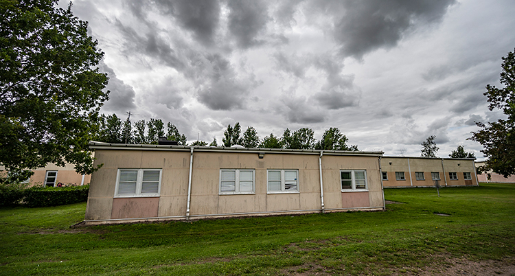 Bild på en skola. Runt skolan är det gräsmatta och träd. Det är mörka moln på himlen.