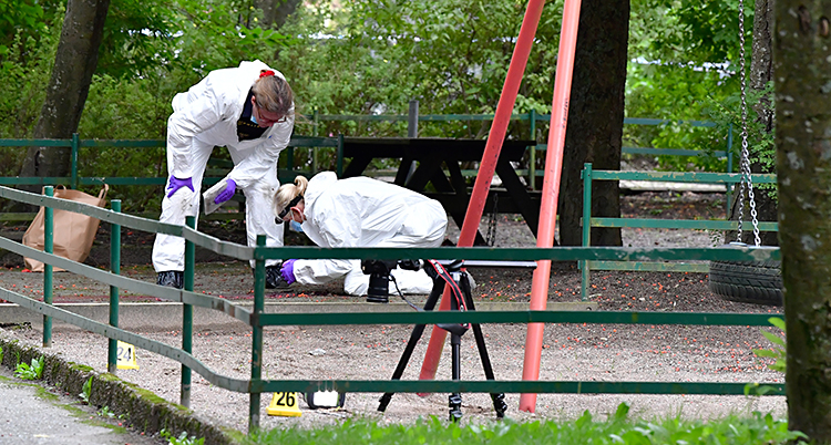 Bilden är tagen utomhus vid en lekplats. Två tekniker från poliserna jobbar med att leta spår. De har på sig vita overaller.