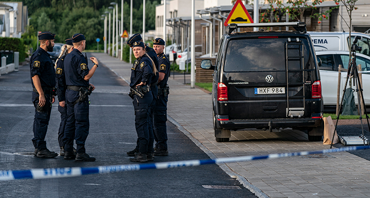 Poliser står på en gata och pratar. Bredvid dem stor en svart bil. Den tillhör polisens tekniker.