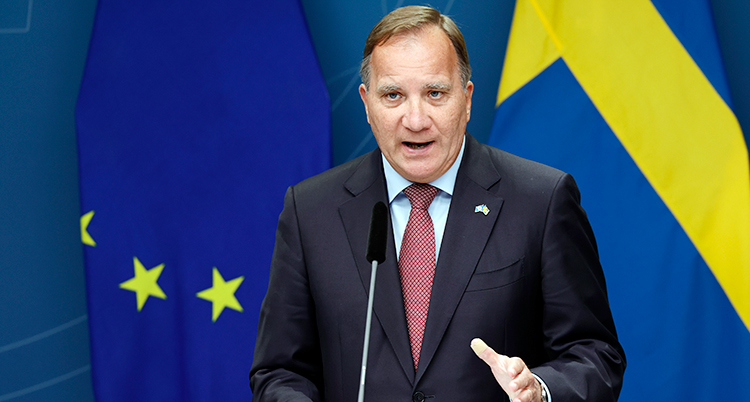 Löfven talar och gör en rörelse med handen. Svenska flaggan är bakom honom.
