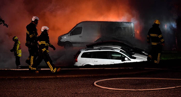 Det är mörkt. Lågor och rök syns. Bilar och brandmän.