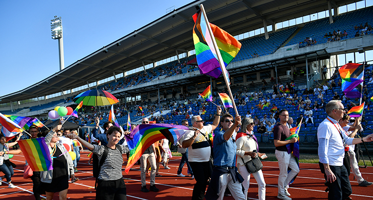 Människor går in på en idrottsarena med prideflaggor i händerna.
