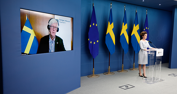 Amanda Lind står och pratar i en mikrofon. Bredvid henne finns en stor skärm. Där syns Johan Carlson.