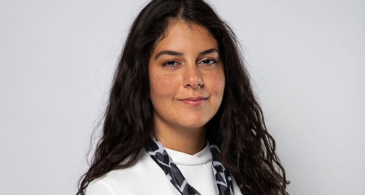 Hon tittar in i kameran. Hon har mörkt hår och vit tröja.