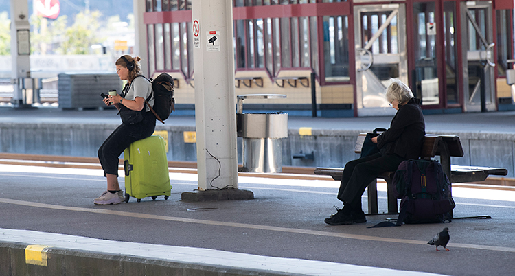 Två personer sitter och väntar på ett tåg. De har resväskor.
