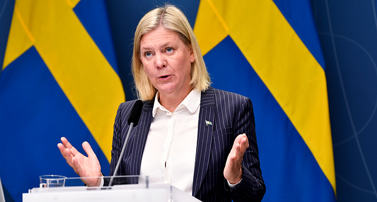 Hon talar i en mikrofon. Bakom henne syns Sveriges flagga.