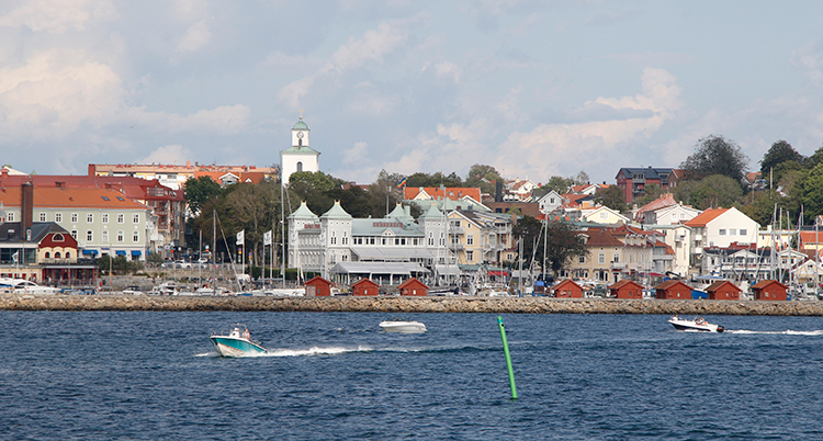 en båt kör i vattnet framför en stad med hus, träd och hamnbodar