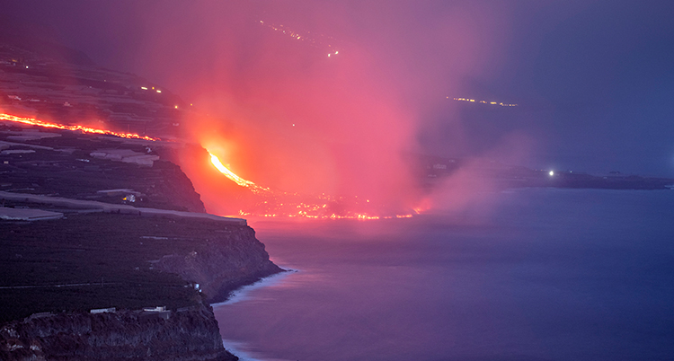 Röd lava rinner ner genom bergssluttningen och ut i havet