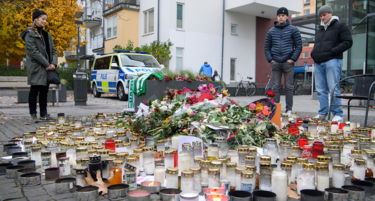 Tre personer runt en stor hög med blommor och ljus.