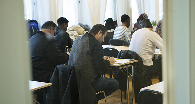 Ett klassrum. Människor sitter vid bänkar.