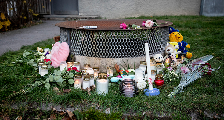 Blommor, ljuslyktor och gosedjur som folk har lämnat på en gräsmatta utanför ett hus.