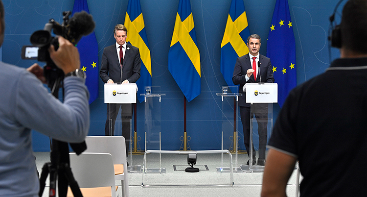 Två ministrar på podiet framför journalister.