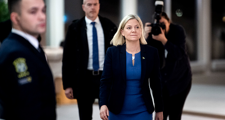 Hon går mot kameran. En vakt står till vänster, en fotograf med kamera bakom.