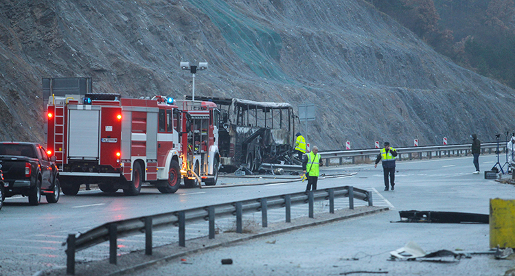 En röd räddningsbild står bakom bussen. Bussen är svart efter branden.