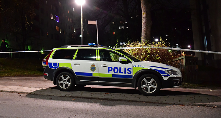 Det är mörkt. En polisbil står parkerad på vägen.