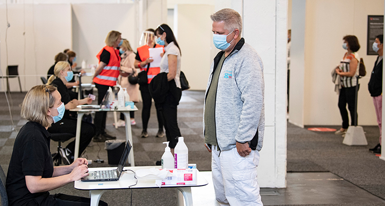 En man köar för att få vaccin. Alla runt honom har munskydd.