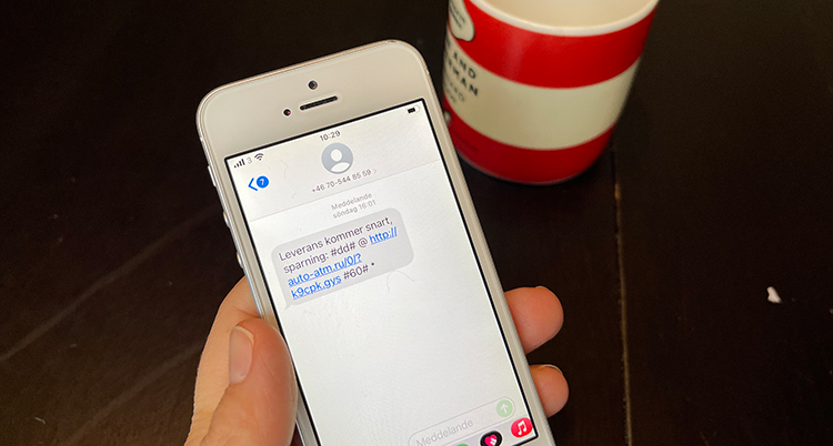 en hand håller en mobil med ett sms om ett paket och en blå länk.