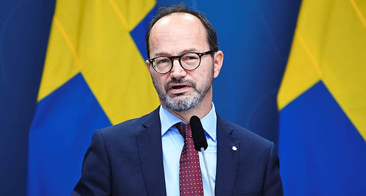 Han står och pratar i en mikrofon. Bakom honom finns svenska flaggor.