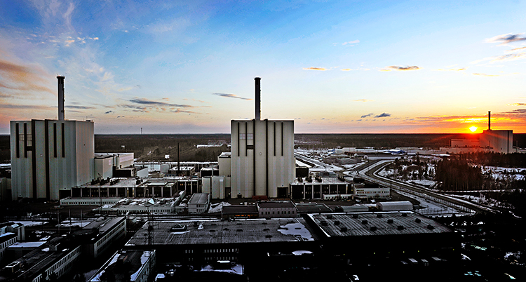 Flera stora byggnader. Blå himmel. Solen ligger i horisonten.