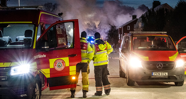 Ambulanser och brandbilar framför några hus. Rök i bakgrunden.