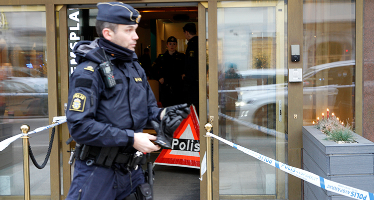 En polis står utanför en entré av glas. Det är avspärrningsband intill.