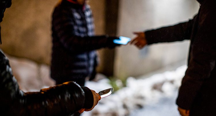 Tre unga står i grupp. En blir vingad att ge sin telefon till en annan. Inga ansikten syns.