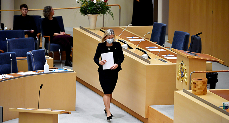 Hon är i riksdagens stora sal och går upp för att tala. Hon har munskydd på sig.
